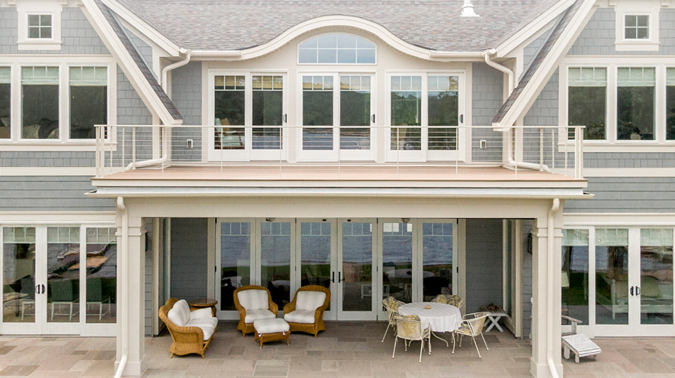 front of a grey house with a terrace on the second floors and sitting spaces below